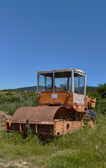 Obraz premium Abandoned vintage road roller in a grassy field with clear blue sky and distant hills visible in the background