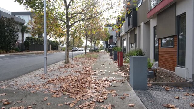 A quiet residential street in Caroline Springs, Melbourne Australia in autumn. Fallen  leaves carpet the footpath. Modern townhouses and medium-density dwellings with contemporary facades.