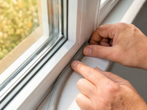 Climate solution: hands installing gray foam weatherstrip along a window sill, showing home insulation, draft sealing, energy saving, winter preparation, and DIY maintenance.