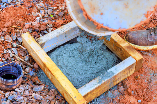 Worker pours concrete from container into wooden mold at construction site during work hours.