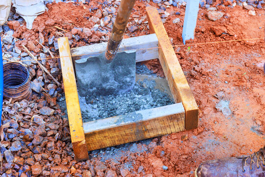 Workers set shovel in wet cement inside wooden frame at construction site