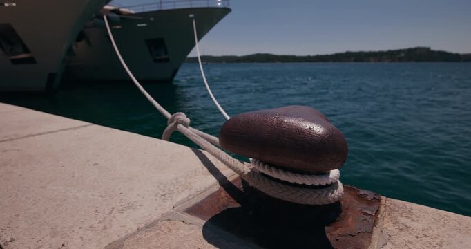 Close up view of a mooring bollard with ropes and a yacht docked on the waterfront in Sibenik, Croatia.