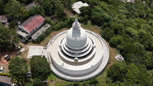 Aerial view of the Japanese Peace Pagoda - Rumassala with people walking on the circular terrace surrounded by lush forest in Unawatuna, Southern Province, Sri Lanka.