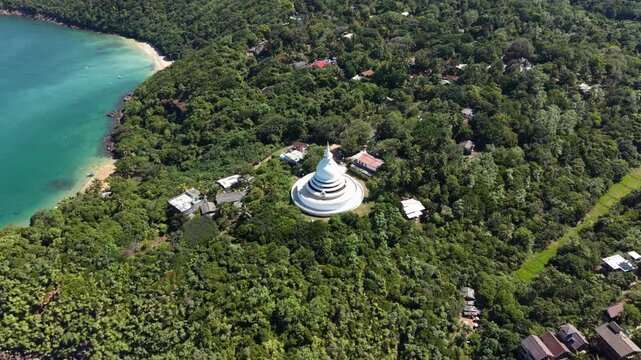 Aerial view of the Japanese Peace Pagoda - Rumassala surrounded by lush tropical forest and the turquoise ocean in Unawatuna, Southern Province, Sri Lanka.
