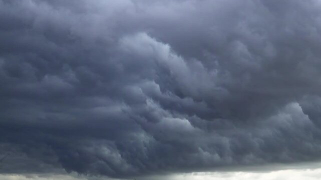 Thick layers of dark grey storm clouds swirling across the whole sky creating a dramatic and ominous atmosphere before heavy rain