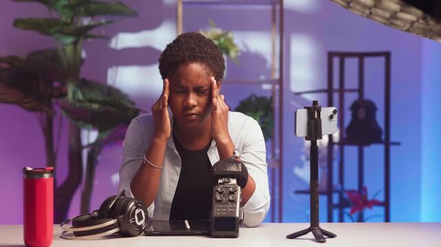 Young African female content creator feeling overwhelmed with a migraine in a home studio