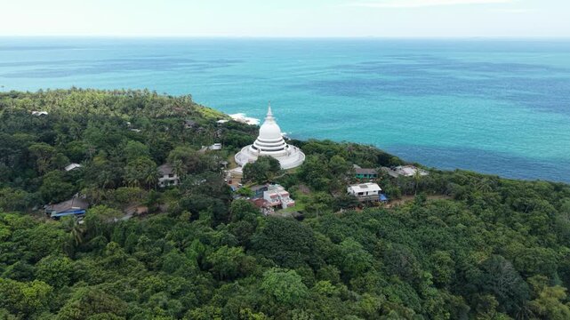 Aerial view of Japanese Peace Pagoda - Rumassala on a lush green hill overlooking the turquoise ocean in Unawatuna, Southern Province, Sri Lanka.