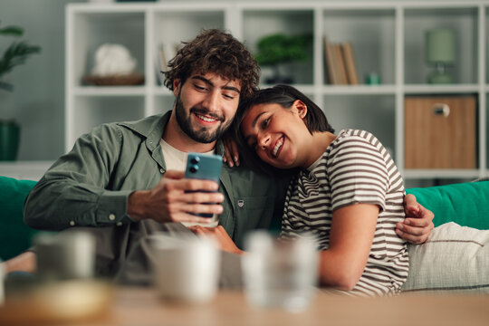 Happy couple relaxing on sofa sharing smartphone content, smiling while enjoying social media and connection at home