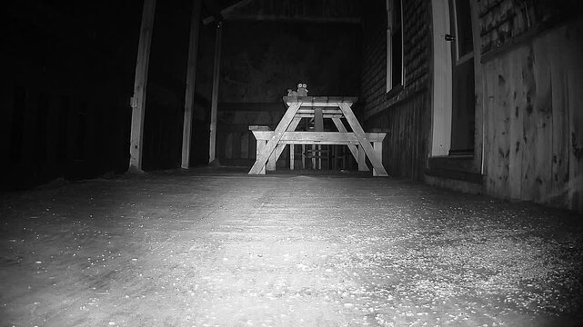 Infrared night vision footage showing a cautious mouse circling beneath a picnic table on a wooden deck near an entrance door during nighttime.