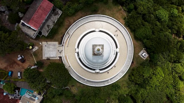 Aerial view of Japanese Peace Pagoda - Rumassala with its white dome and people walking on the circular walkway surrounded by forest Unawatuna, Southern Province, Sri Lanka.