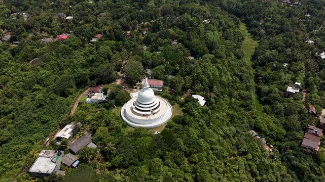 Aerial view of the white Japanese Peace Pagoda nestled within the dense tropical forest of Rumassala in Unawatuna, Southern Province, Sri Lanka.