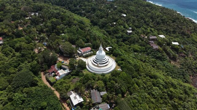 Aerial view of the white Japanese Peace Pagoda - Rumassala surrounded by dense tropical forest and coastal greenery in Unawatuna, Southern Province, Sri Lanka.