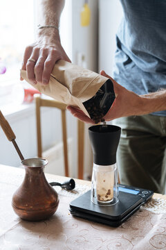 Crop man spilling coffee into grinder