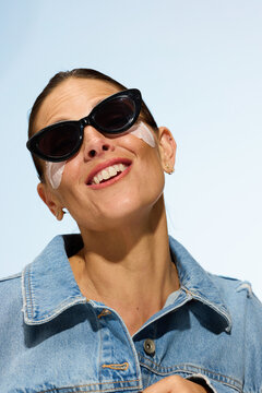 Woman Applying Skincare and Smiling in Bright Sunlight