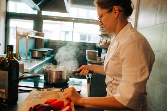 Chef cooking with steaming pot on stove in professional kitchen