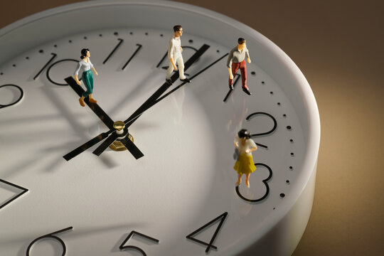Miniature people figurines walking on a white analog clock