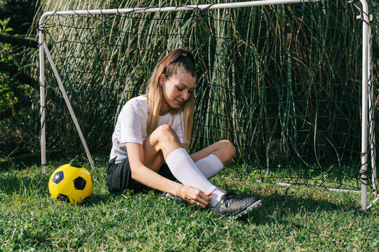 Young Woman Soccer Player Tying Cleats in Backyard Goal