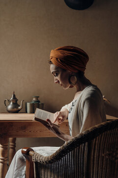 Concentrated woman in turban reading in armchair