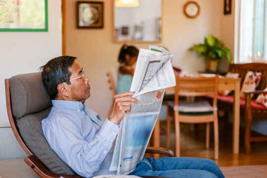 Grandfather reading newspaper next to granddaughter