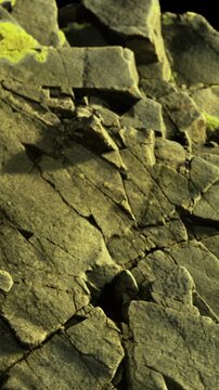 Rocks are visible on a cliff with sunlight shining on the surface. Cracks and textures are present throughout the rocks creating a natural pattern. The scene shows a solid formation.