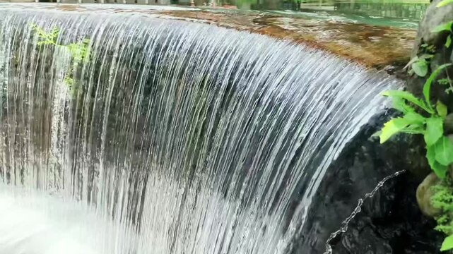 Flowing water over small dam or waterfall structure, natural freshwater movement creating relaxing and peaceful scenery.