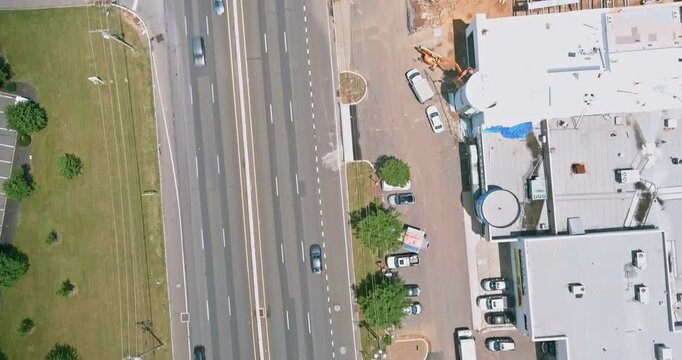 Cars drive along busy highway with commercial building on parking spaces are filled near building while present in surrounding area.