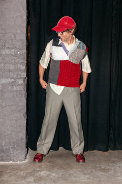 Man wearing a colorful vest and cap stands in a dimly lit space