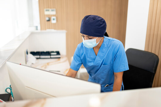 Nurse working at reception desk wearing surgical mask and scrubs
