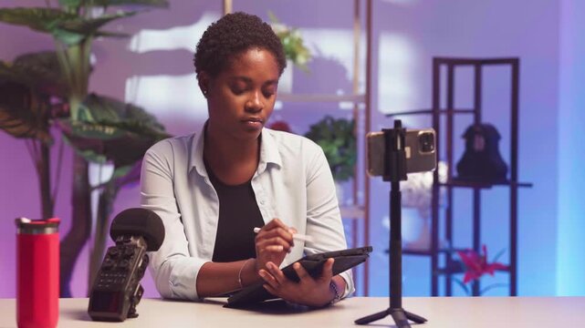 Young African woman creating digital content in a studio setup with a tablet and smartphone