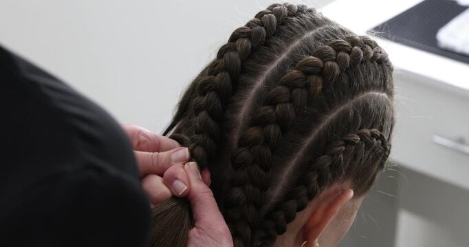 Hairstylist braiding teenage girl's hair in salon, closeup