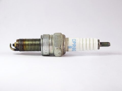 Used motorcycle spark plug isolated on white background, showing electrode wear and threaded metal body, a crucial ignition component for automatic CVT engine performance.