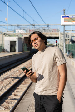 Young man waiting for train using smartphone at station