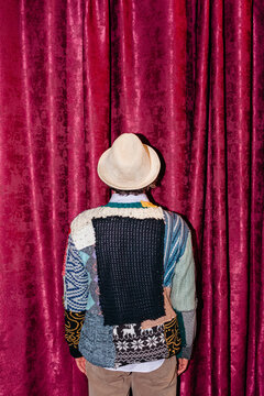 Man stands facing a maroon curtain while wearing a vintage sweater