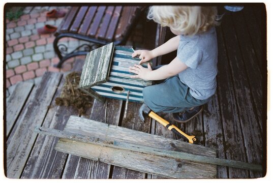 A baby boy is repairing a birdhouse.