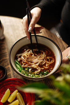 Woman Holding Bowl of Beef Noodle Soup with Chopsticks