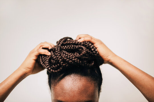 Crop of anonymous african faceless woman braiding her hair in a bun