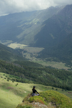 Person sits on cliff edge overlooking green mountains and valley