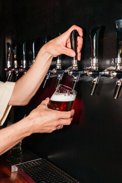 Bartender pours beer into glass at tap in a bar during evening hours