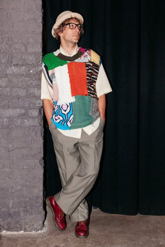 Man stands by wall in creative outfit with patchwork design