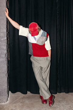 Fashion show model poses in unique outfit against black curtain