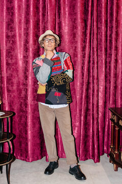 Man stands in front of red curtain wearing colorful sweater