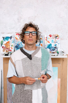 Artist stands in studio holding paint tube