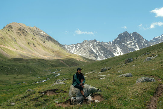 Hiker resting on a rock in a green valley with mountains