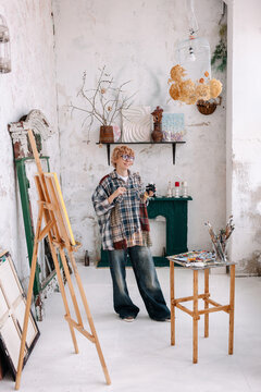 Artist in a studio preparing to paint with supplies and easel