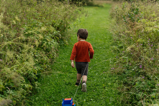 Child walking on grassy path pulling toy truck