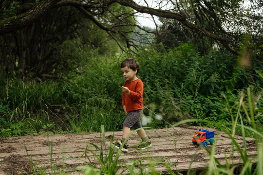 Child pulling toy truck on wooden path in forest