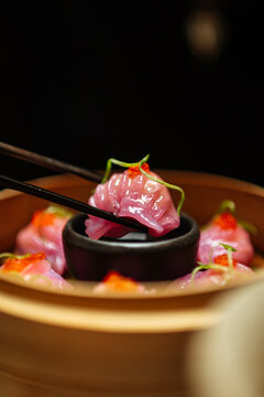 Pink dumpling held with chopsticks above dipping sauce