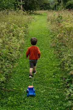 Child walking on grassy path pulling toy truck