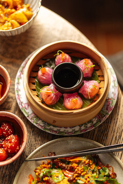 Purple dumplings with dipping sauce in bamboo steamer on wooden table