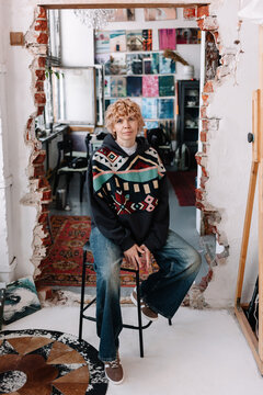 A female artist sits on a stool in a creative workspace